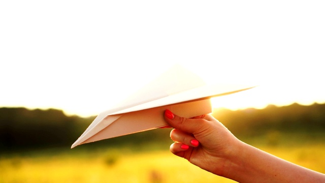 在橙色的夕阳下，女人手握白纸飞机。自由的概念视频素材