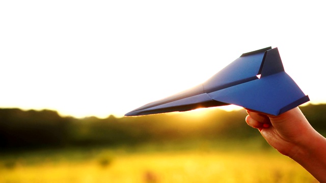 一个面目全非的女人在如画的日落背景上玩纸飞机视频素材