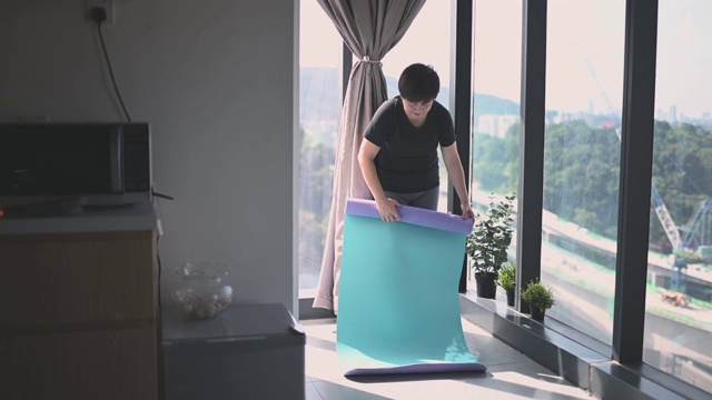 周末的早上，一位中国美女在厨房靠窗的角落里滚动瑜伽垫，在家锻炼身体视频素材
