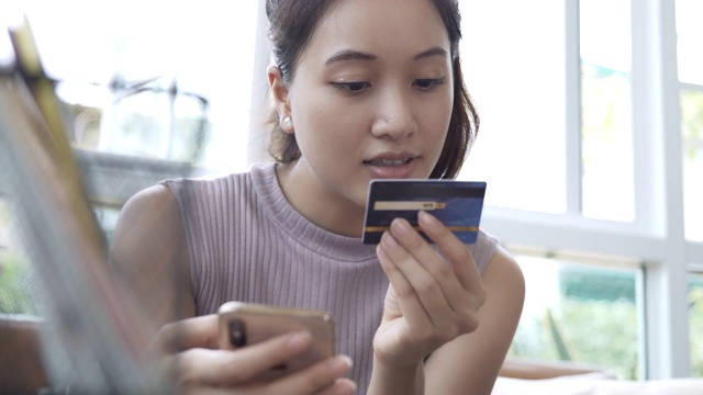 年轻女子在家里用手机刷信用卡购物的场景视频素材
