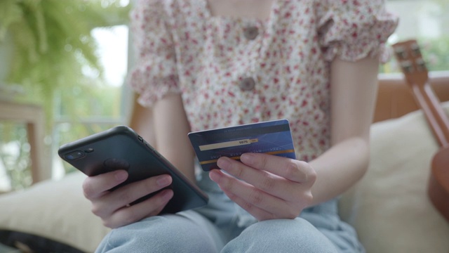 年轻女子在家里用手机刷信用卡购物的场景视频素材