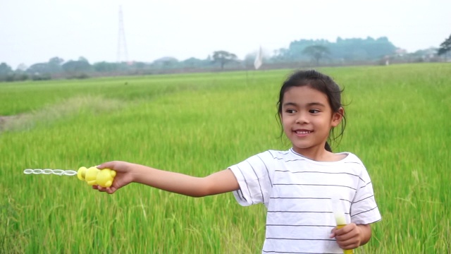 亚洲的孩子们笑着，在夏天的绿色稻田里吹泡泡。视频素材