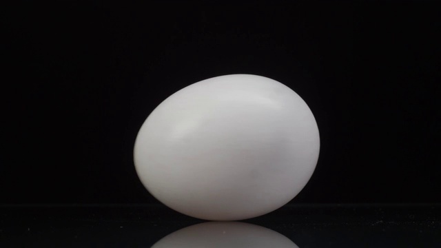 白色的鸡蛋在黑色的背景上纺纱滚动，有着美丽的倒影。近距离视频下载