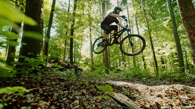 超级SLO MO MTB摩托车手跳过一个木斜坡在阳光明媚的森林视频素材