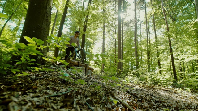 超级SLO MO MTB摩托车手跳过一个木斜坡在阳光明媚的森林视频下载