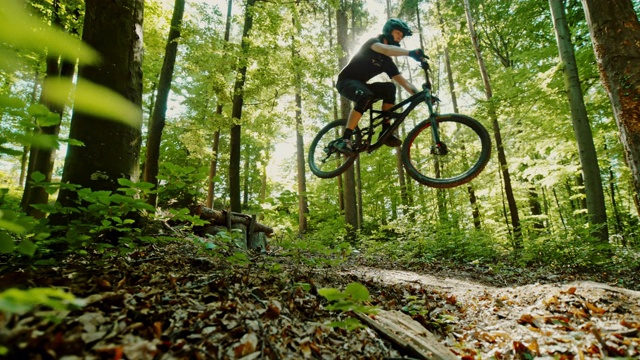 超级慢动作时间扭曲效果MTB摩托车手跳过一个木斜坡在阳光灿烂的森林视频素材
