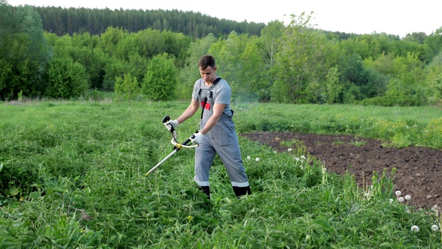 穿着灰色工作服的人在田里用剪草机割荨麻视频下载