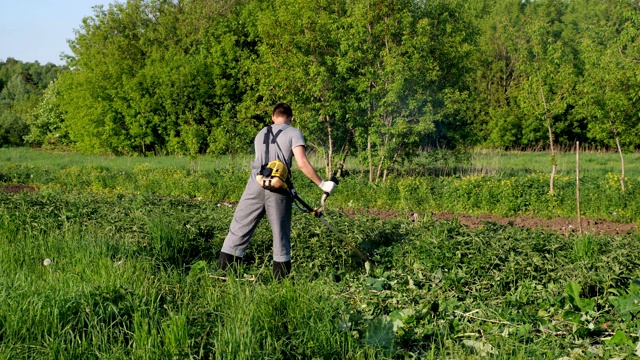 穿着工作制服的英俊男子正在用修剪机修剪草坪。从后面看视频下载