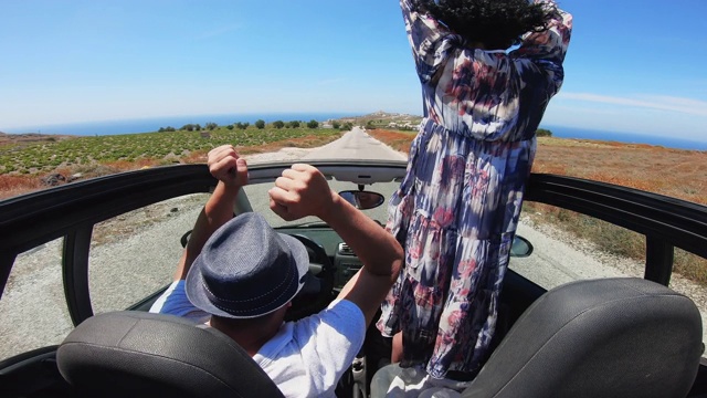 一对夫妇驾驶敞篷车，用稳定器拍摄。新婚夫妇在浪漫的希腊圣托里尼岛度蜜月视频素材