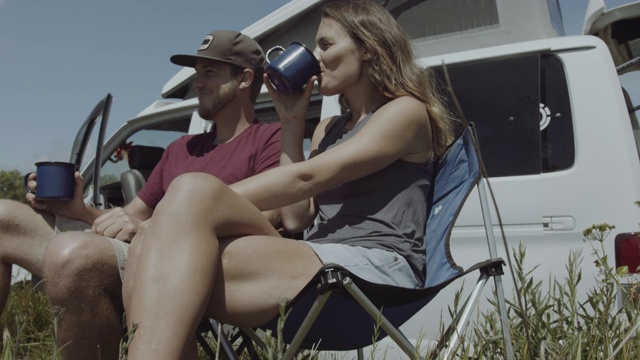 年轻的成年夫妇在公路旅行谈话和喝咖啡外露营在夏季逃跑视频素材