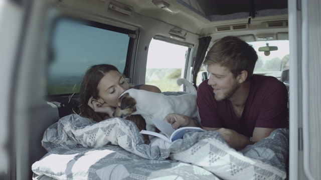 年轻的成年夫妇一起在床上公路旅行在露营车里看书和玩狗视频素材