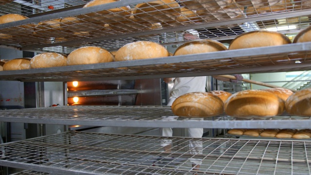 厨师将新鲜烘焙的面包制品从烤箱中取出。烘好的面包是从面包店的烤箱中取出来的。视频下载