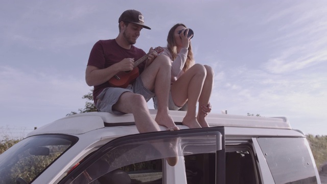 年轻的成年夫妇坐在屋顶露营车欣赏风景和播放音乐视频下载