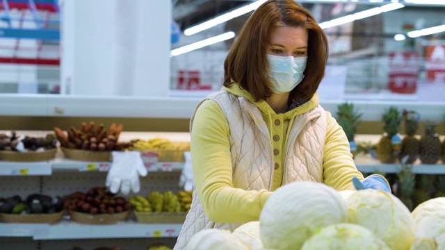 戴着医用口罩的购物者在流行病期间在杂货店里采摘卷心菜视频素材