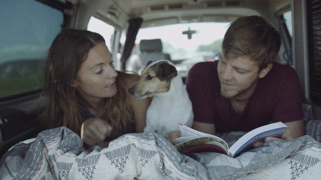 年轻的成年夫妇一起在床上公路旅行在露营车里看书和玩狗视频素材