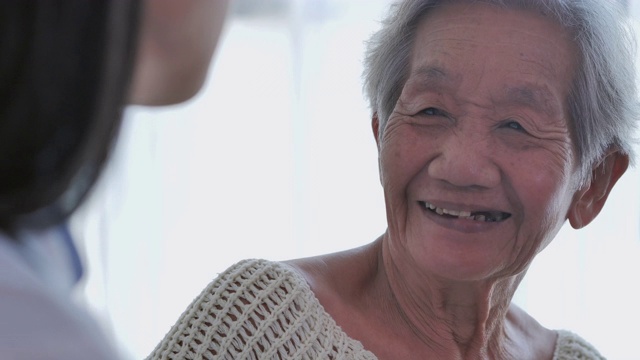 亚洲老年妇女听亚洲年轻女护士医生在咨询和手握她的年长女性病人在家。在家里照顾者视频下载