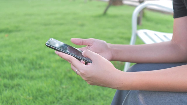 照片中，一名年轻女子在花园里用智能手机的触摸屏打字。也有4K分辨率。视频素材