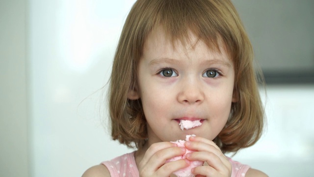 小可爱的3岁女孩吃愉快的粉红色棉花糖，看着相机，微笑和大笑。视频素材