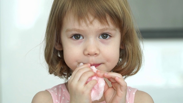 小可爱的3岁女孩吃甜的粉红色棉花糖的特写，看着相机，微笑和大笑。视频下载