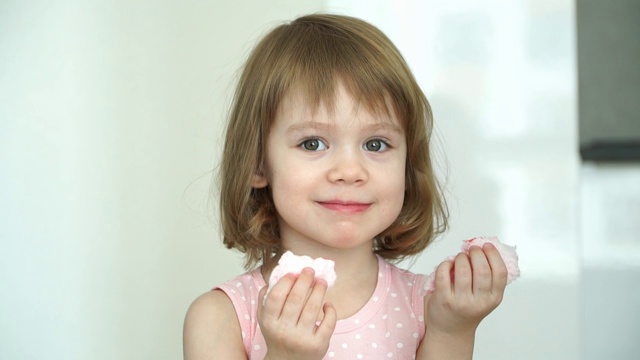 一个有趣的3岁小女孩开心地吃着粉红色的棉花糖，看着相机，笑着。视频素材