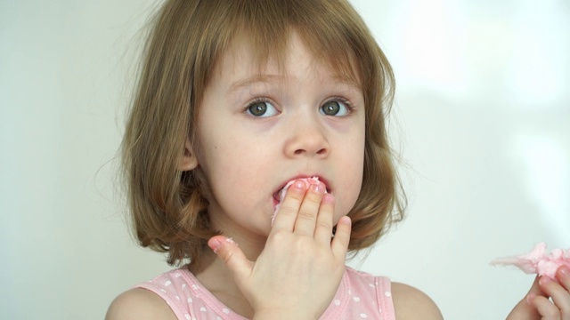 一个有趣的3岁小女孩吃着粉红色的棉花糖看着镜头，笑了起来。视频素材