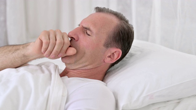 生病的中年男子躺在床上咳嗽视频素材