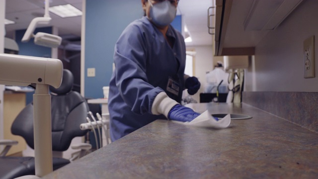 一名50多岁的拉丁裔牙科保健师戴着口罩擦拭检查室周围的柜台和各种表面，为下一个病人做准备视频素材