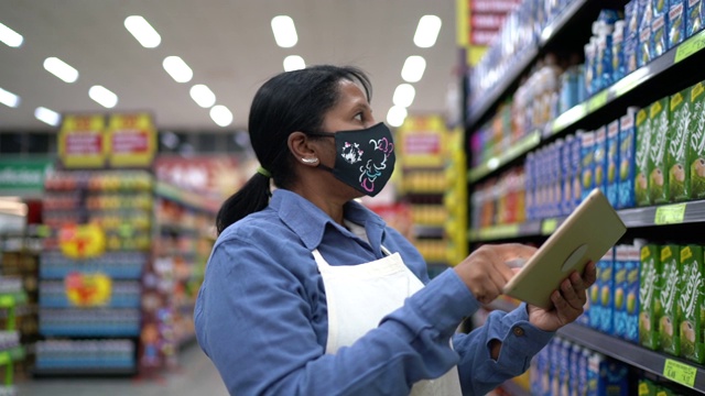 女超市员工或老板戴口罩行走和使用平板电脑视频素材