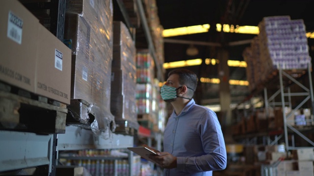 在仓库里，戴着口罩行走和使用平板电脑的人视频下载