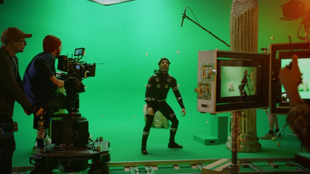 导演命令摄像机操作员开始拍摄绿色屏幕CGI场景与演员穿着运动跟踪服和头部钻机。大电影工作室专业摄制组拍摄大片视频素材