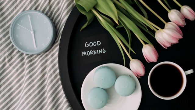 6点钟:托盘上的“早上好”，配有法国马卡龙、新鲜郁金香、一杯咖啡和闹钟视频下载