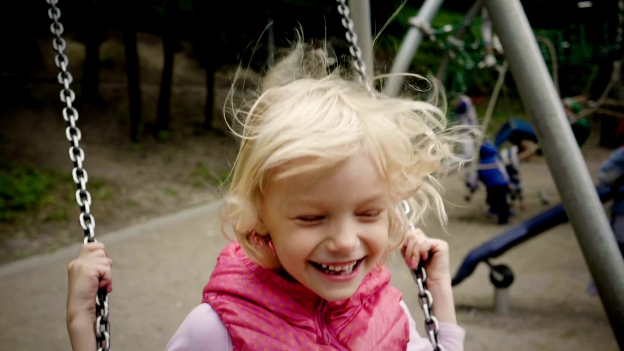 一个积极微笑的小女孩一边笑一边荡秋千。缓慢的运动。高清视频下载