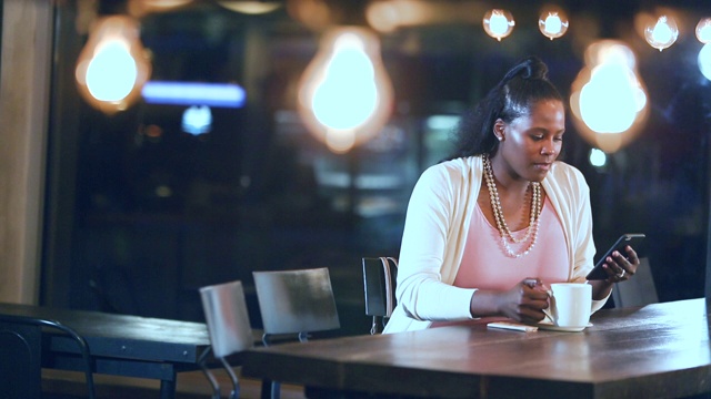 非裔美国女人喝着咖啡，用着智能手机视频素材