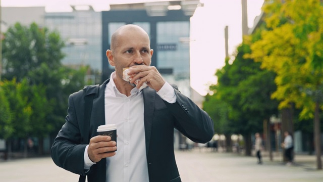 生意人一边吃着汉堡一边喝着咖啡走在城市里视频素材