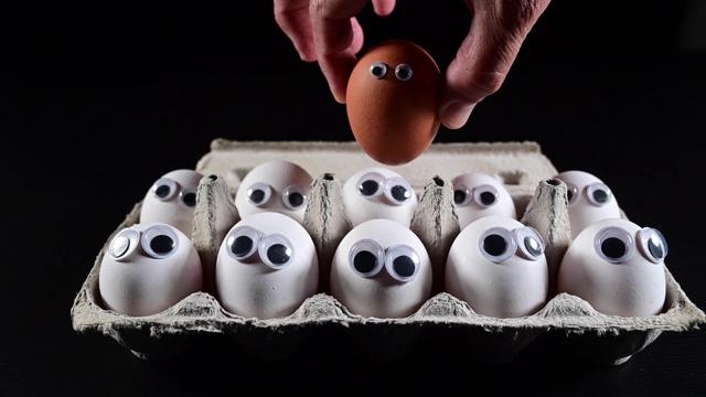 一个男人的手拿着一个棕色的鸡蛋，但是装满了白色鸡蛋的盒子里没有更多的地方了。视频下载