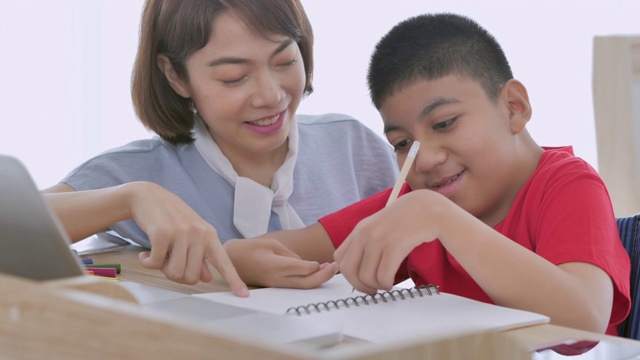 亚洲青少年男孩残疾在轮椅学习，写在线课堂从家里和亚洲年轻女性护理帮助患者教育平板电脑在家。视频下载