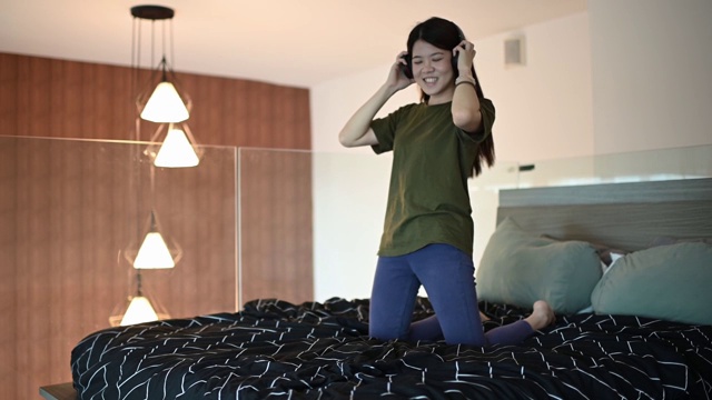 一个美丽的亚洲中国长发年轻女子听和享受音乐在她的床上与她的耳机视频素材