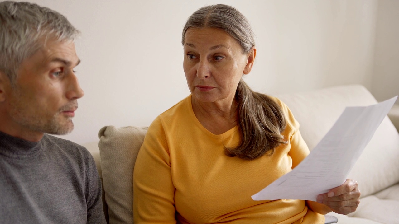 倾斜中镜头的老夫妇坐在沙发上，在家里计算家庭财务。退休夫妇讨论账单和争吵视频下载