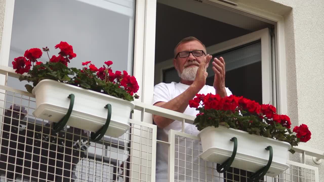 全球大流行期间，胡子花白的老人在阳台上鼓掌支持医护人员。社交距离和自我隔离视频下载