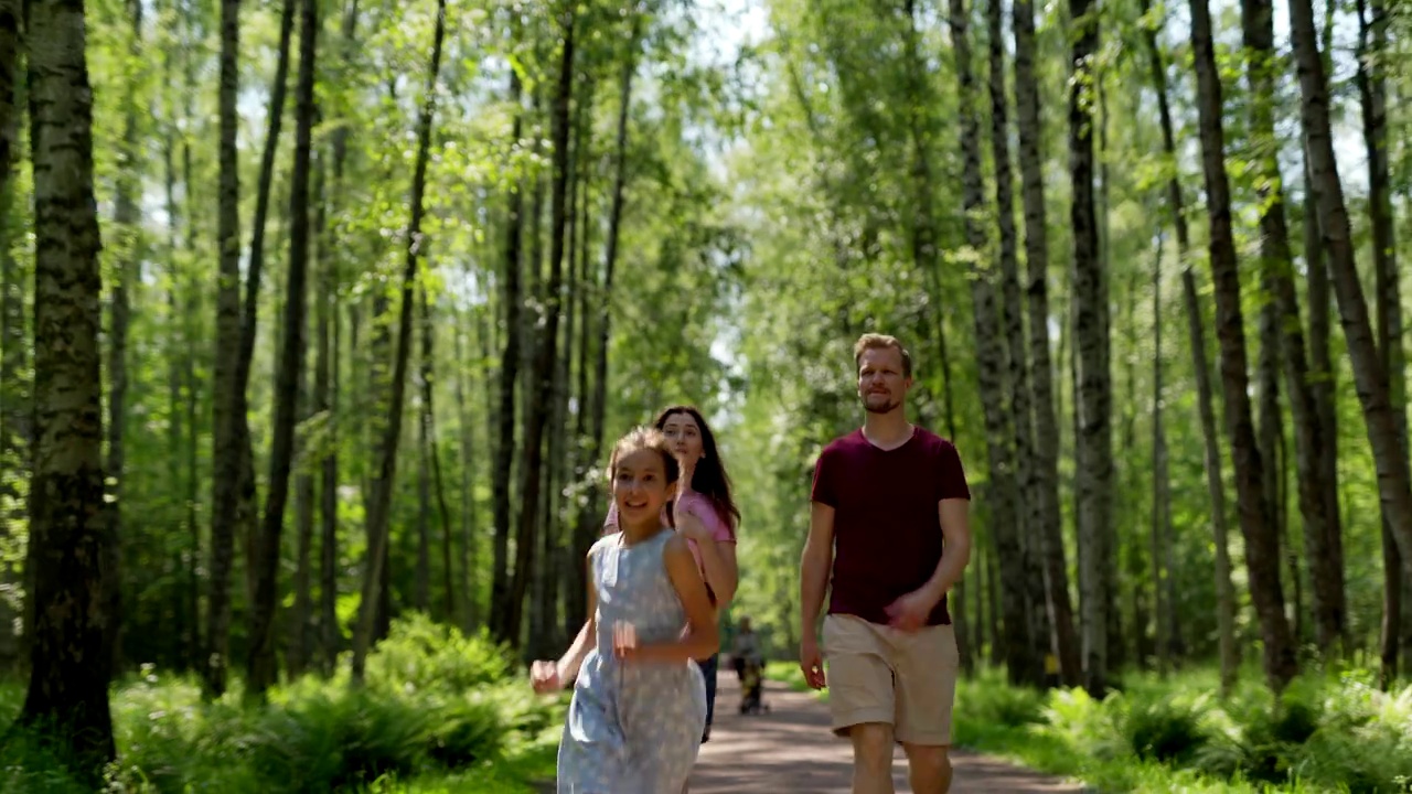 幸福的家庭，母亲，父亲和女儿享受聊天和散步在绿色公园的步道。一家人看着周围的大自然。兴奋的女孩指着某样东西向前跑视频下载