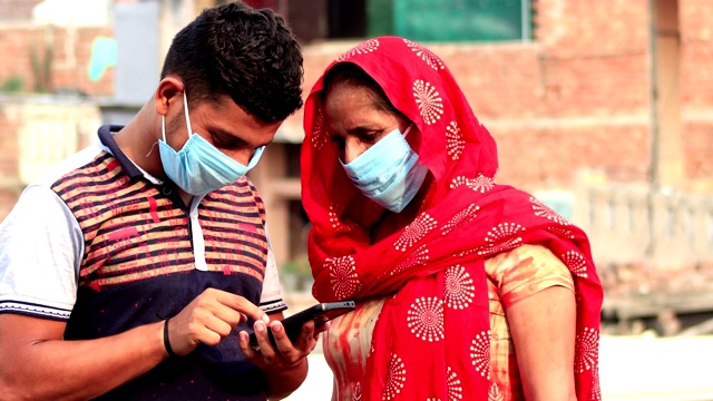 妇女们戴着防病毒的污染口罩，和儿子一起使用智能手机视频素材