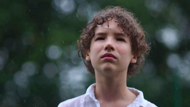 一个悲伤的卷发少年的特写站在倾盆大雨中。青少年心理问题概念视频下载