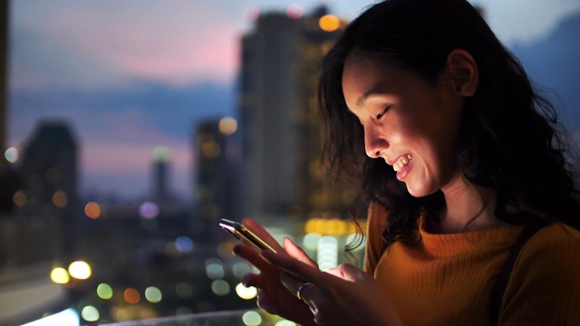 年轻的亚洲女人在城市的夜晚使用智能手机视频素材