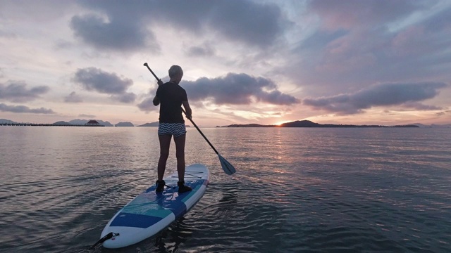 一个女人在海上学习划桨，美丽的日出视频下载