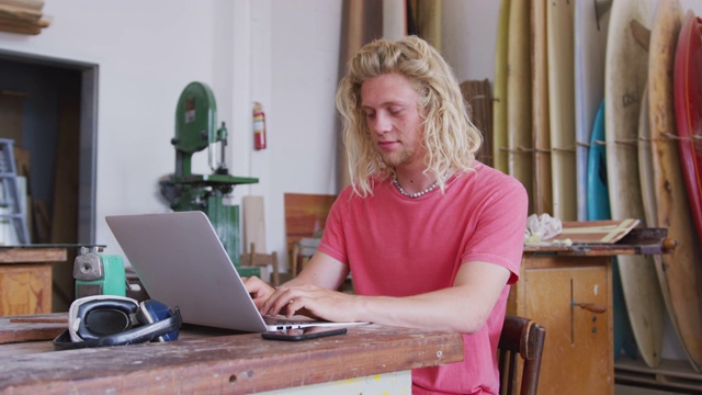 白人男性冲浪板制造者在他的笔记本电脑上工作视频下载