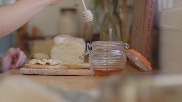 一名年轻女子将蜂蜜滴在厨房柜台上的新鲜面包上视频素材