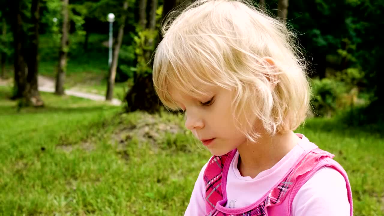 在夏日公园里，金发小女孩一边吃饭一边点头。4 k视频下载