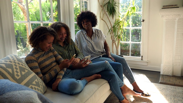母女俩坐在客厅的沙发上笑着看智能手机视频下载