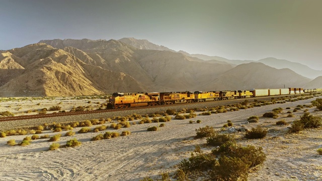 WS航空跟踪货运列车与五个柴油发动机牵引货物在无标记的货运车厢通过沙质南加州沙漠地形对圣戈尼奥山视频下载