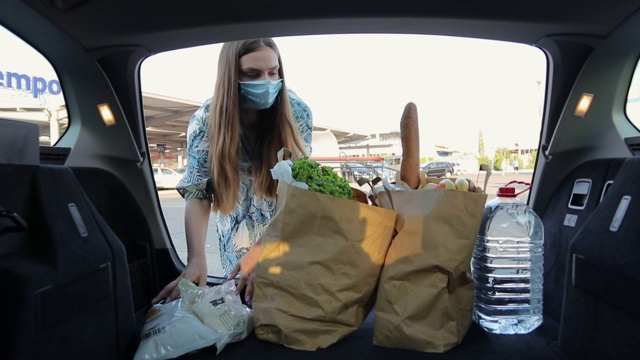 年轻女子戴着防护面罩，在汽车后备箱里装杂货视频下载
